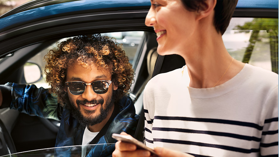 BMW Connected En mann i BMW og en kvinne utenfor bruker BMW Connected på smarttelefonen