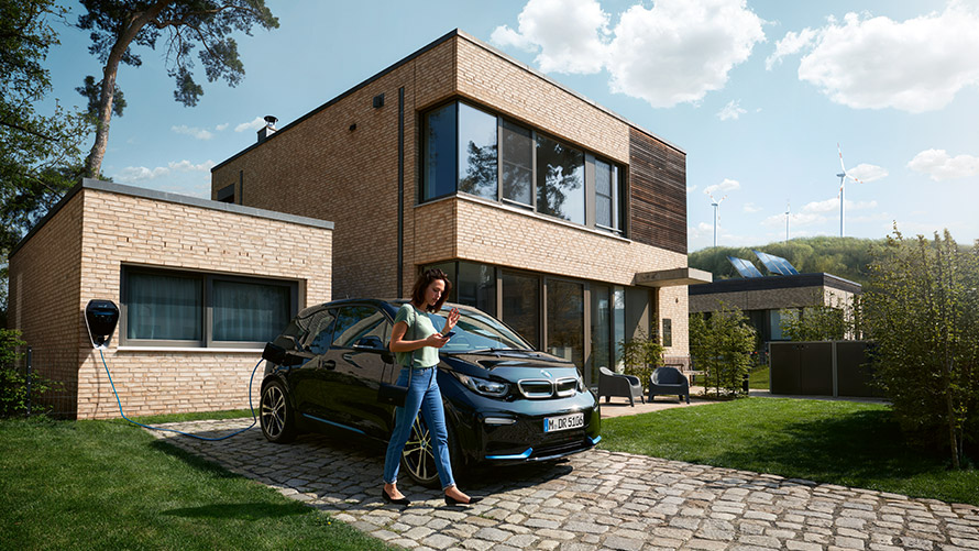 Digital Charging Service Kvinne går foran en BMW i3 og bruker Digital Charging Service på smarttelefonen
