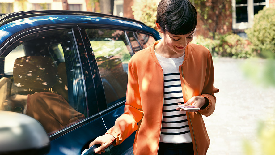 BMW Teleservices Kvinne med smarttelefon står i døra til sin BMW