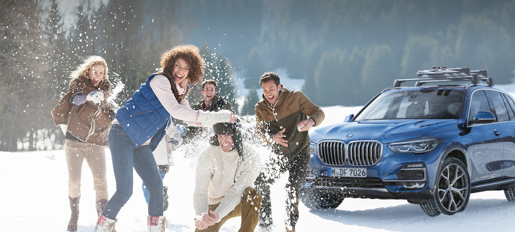 BMW Originaltilbehør og BMW service for vinteren Kvinner og menn som ler i snøen foran en BMW