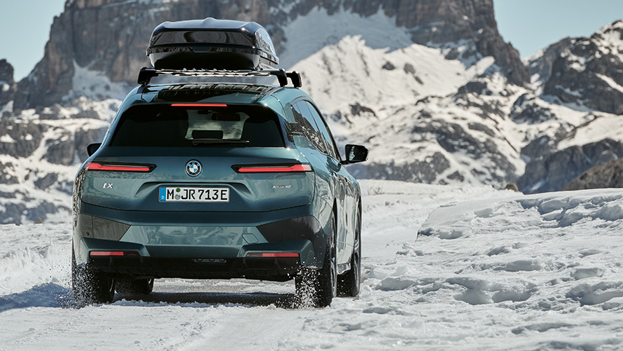 BMW komplette vinterhjul på BMW iX (I20) på snødekt vei foran fjell BMW komplette vinterhjul på BMW iX (I20) på snødekt vei foran fjell