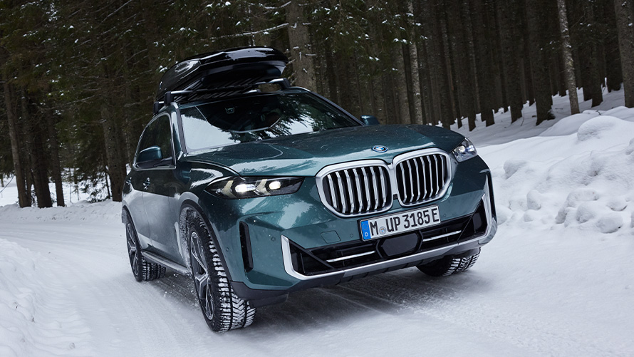 BMW komplette vinterhjul på BMW iX (I20) på snødekt vei foran fjell BMW komplette vinterhjul på BMW iX (I20) på snødekt vei foran fjell