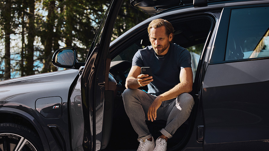 Mann sitter i en BMW og ser på smarttelefonen sin BMW vår- og sommertilbehør Mann sitter i en BMW og ser på smarttelefonen sin