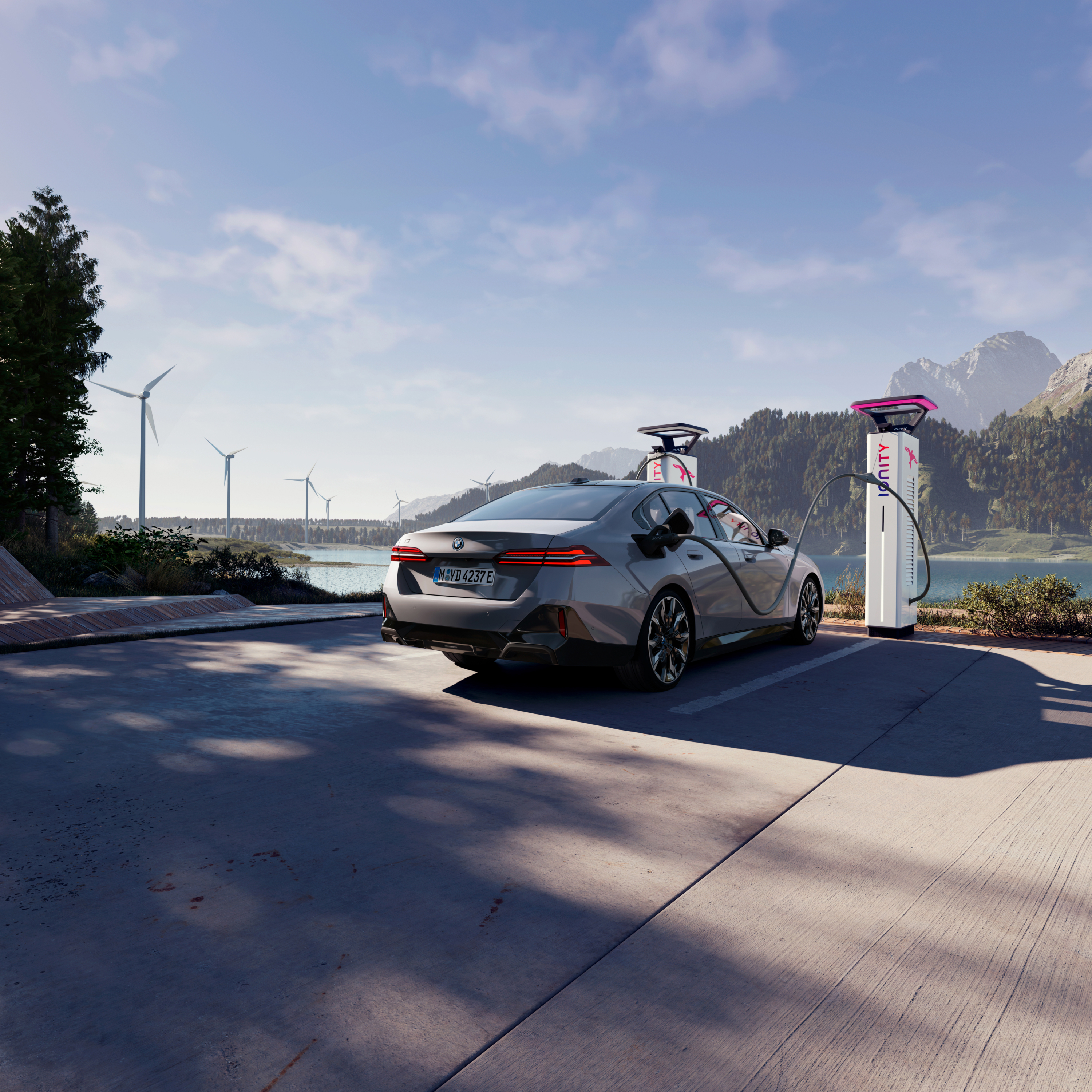 BMW lader ved en ladestasjon med utsikt over vann, fjell og vindturbiner